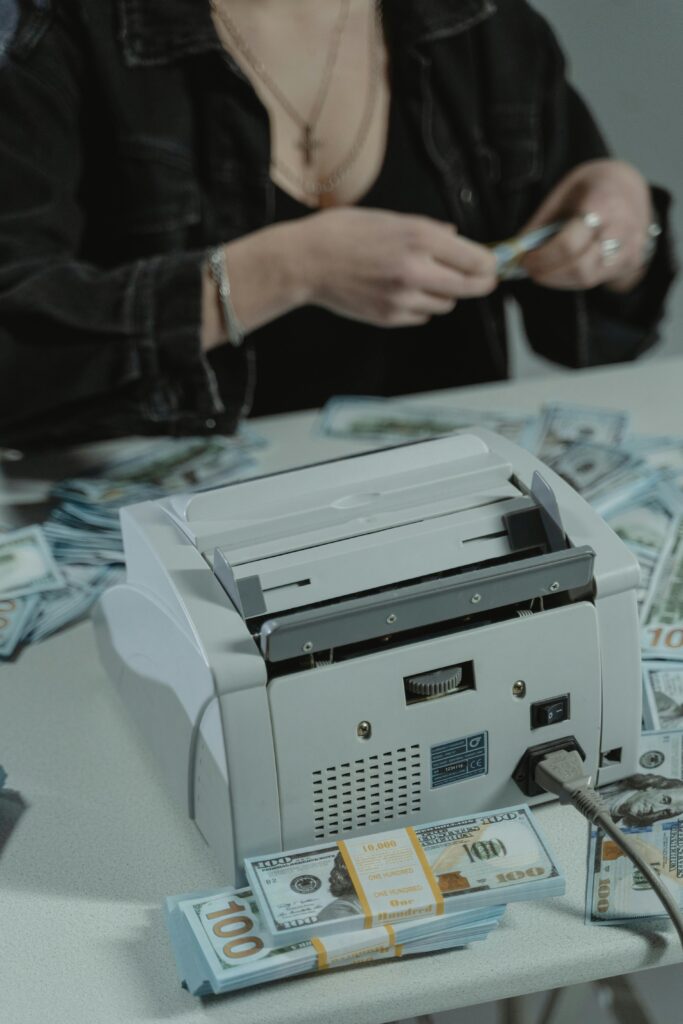 Woman using a money counter to count US dollar bills on a table.