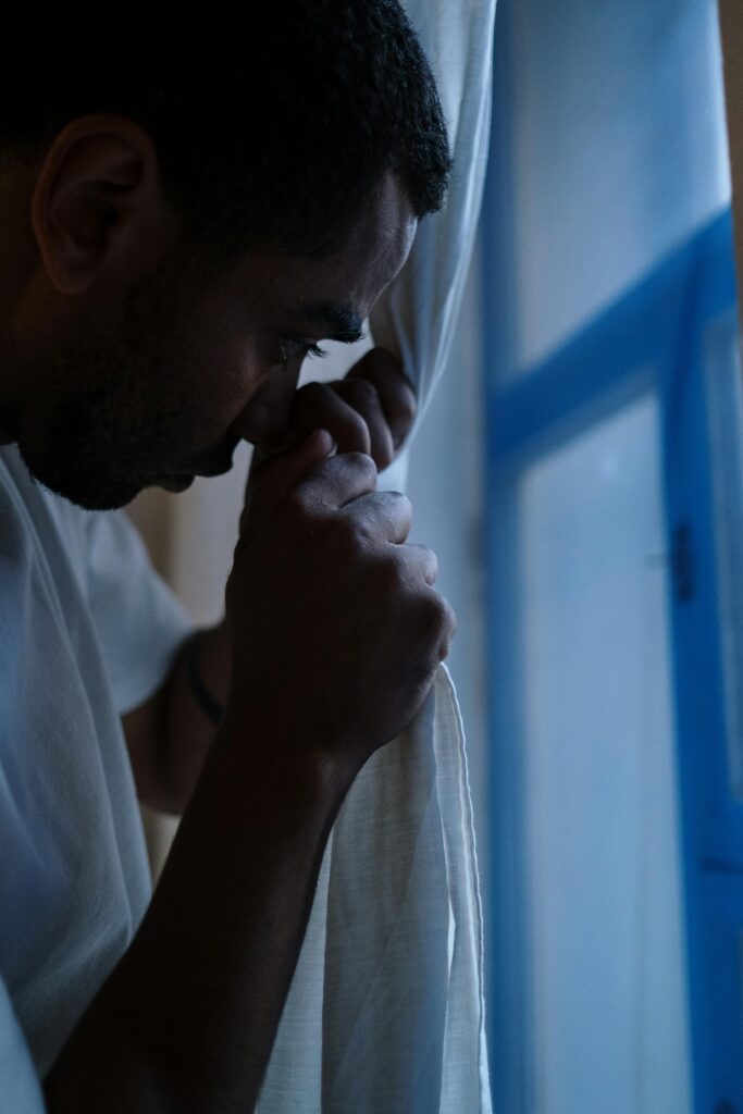 A man in deep thought peeping through curtains at home, depicting solitude and introspection.