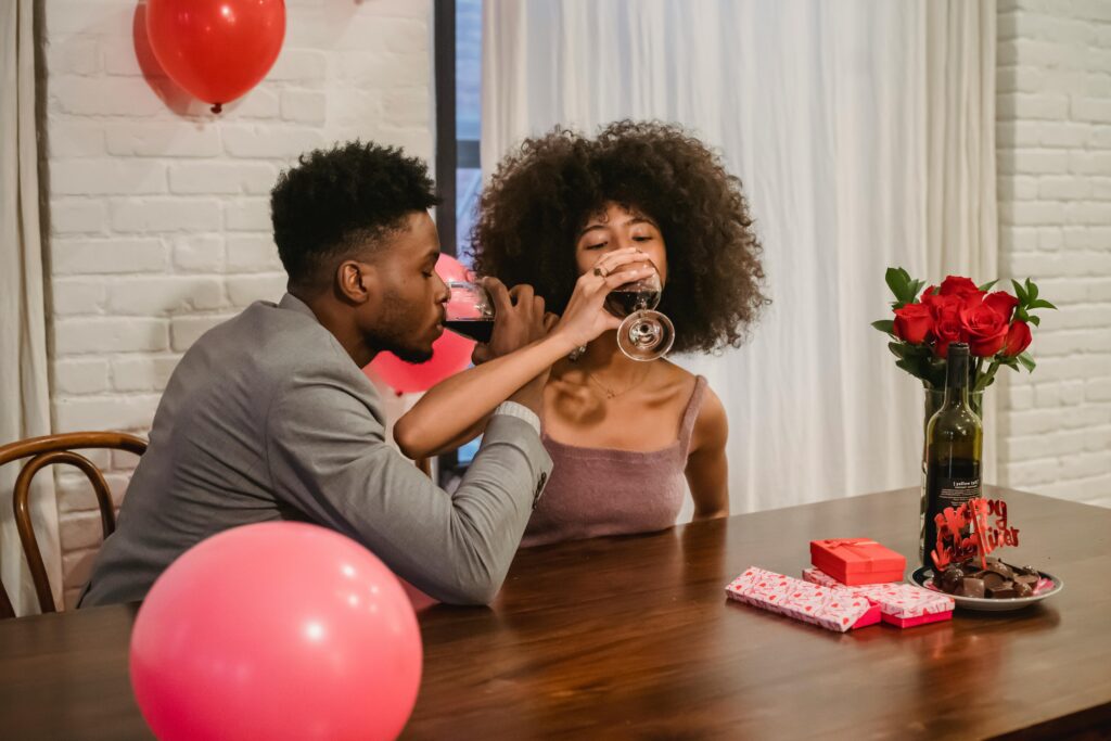Couple enjoying a romantic Valentine's Day celebration indoors with wine and gifts.